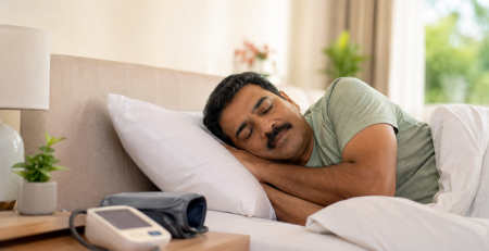 Man sleeping beside a blood pressure monitor, illustrating the link between sleep apnea and high blood pressure.